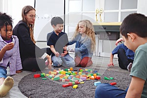 Group of primary school children study and play together in classroom with teacher, diverse students sit on floor while do