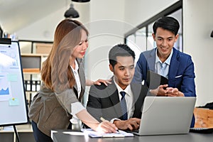 Group of professional Asian businesspeople looking at laptop screen, working together in office