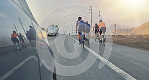 Group of professional cyclists training on highway with safety escort car, security light