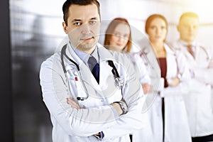 Group of professional doctors, standing as a team with crossed arms in a sunny hospital office, ready to help their