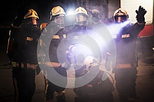 Group of professional firefighters posing. Firemen wearing uniforms, protective helmets and oxygen masks. Smoke and firetrucks