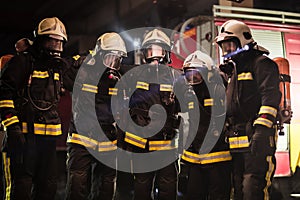 Group of professional firefighters posing. Firemen wearing uniforms, protective helmets and oxygen masks. Smoke and firetrucks in