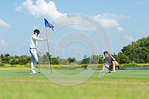 Group Professional Golfer asian man and friend playing aiming shot for putting ball on the hole with club on green course.  Hobby