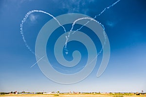 A group of professional pilots of aircraft of fighters on a sunny clear day shows tricks in the blue sky, drawing a romantic heart