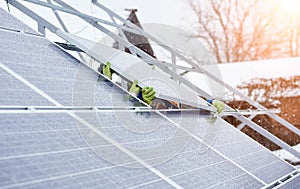 Group of professionals installing photovoltaic solar panels on the roof of modern house during snowy winter time.