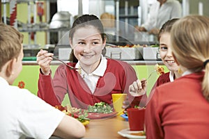 Group Of Pupils Sitting At Table In School Cafeteria Eating Lunc