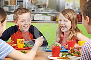 Group Of Pupils Sitting At Table In School Cafeteria Eating Meal photo