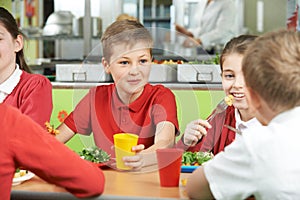 Group Of Pupils Sitting At Table In School Cafeteria Eating Meal photo