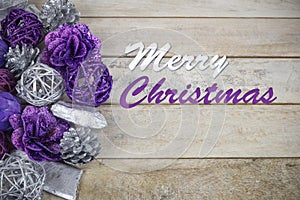 Group of purple and silver Christmas decoration on a wooden background with text in English `Merry Christmas`