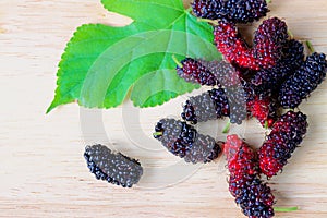 Group of red and black mulberry with leaf on the wooden.