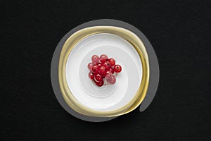 Group of red currants placed on a golden dish with isolated black background