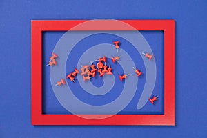 Group of red push pins scattered inside a red frame on blue background isolated