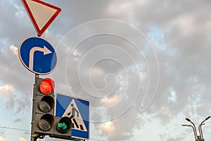 A group of road signs and a traffic light with an additional section at the intersection against the sky. A red traffic light and