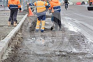 A group of road workers install road curbs along the roadway