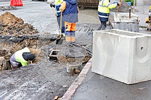 A group of road workers repair sewer storm hatches on a roadway on an autumn day