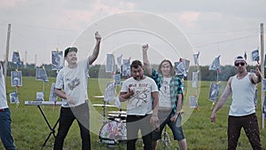 A group of rock musicians explodes simultaneously several firecrackers on the background of their instruments in the field in the