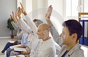 Group of satisfied business people raise their hands to ask questions during business seminar.