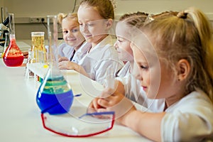 Group of school girl kids with teacher in school laboratory making experiment observing the chemical reaction with the
