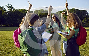 Group of school kids having outdoor lesson and raising hands to answer teacher& x27;s question