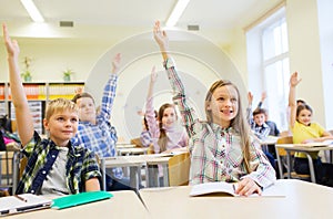 Group of school kids raising hands in classroom