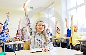 Group of school kids raising hands in classroom