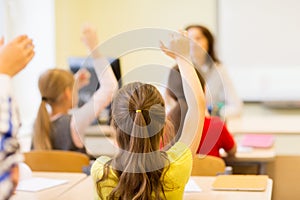 Group of school kids raising hands in classroom