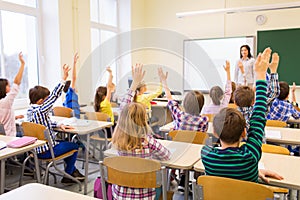 L'educazione, la scuola elementare, l'apprendimento e la gente concetto di gruppo di bambini della scuola con insegnante seduto in aula e alzando le mani.