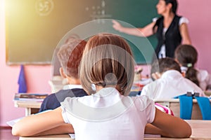 group of school kids sitting and listening to teacher in classroom from back