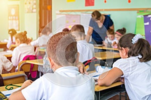 group of school kids sitting and listening to teacher in classroom from back