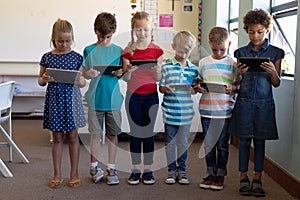 Group of schoolchildren standing in a line and using tablet computers
