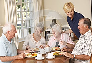 Group Of Senior Couples Enjoying Meal Together In Care Home With