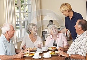 Group Of Senior Couples Enjoying Meal Together In Care Home With Home Help