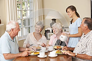 Group Of Senior Couples Enjoying Meal Together In Care Home With Teenage Helper