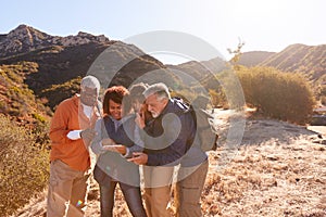 Group Of Senior Friends Checking GPS On Mobile Phone As They Hike Along Trail In Countryside