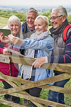 Group Of Senior Friends Hiking In Countryside Standing By Gate  And Taking Selfie On Mobile Phone