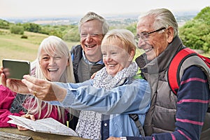 Group Of Senior Friends Hiking In Countryside Standing By Gate  And Taking Selfie On Mobile Phone