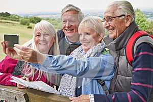 Group Of Senior Friends Hiking In Countryside Standing By Gate  And Taking Selfie On Mobile Phone