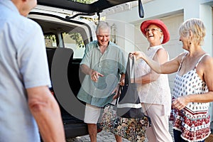 Group Of Senior Friends Loading Luggage Into Trunk Of Car About To Leave For Vacation