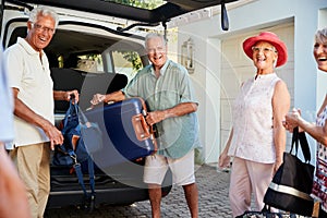 Group Of Senior Friends Loading Luggage Into Trunk Of Car About To Leave For Vacation