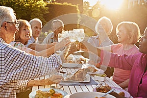 Group Of Senior Friends Making A Toast At Outdoor Dinner Party