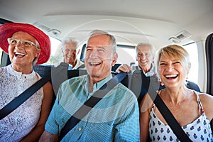 Group Of Senior Friends Sitting In Back Of Van Being Driven To Vacation