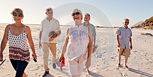 Group Of Senior Friends Walking Along Sandy Beach On Summer Group Vacation