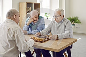 Group of senior men in retirement home sitting at table, playing chess and thinking