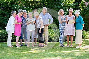 Group of senior people discussing their paintings together with course instructor, while standing in garden on sunny day