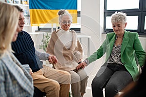 Group of seniors holding hands and praying for Ukraine together in church community center.