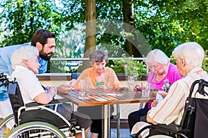 Group of seniors and nurse playing cards in rest home