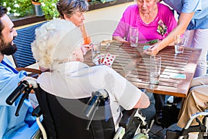 Group of seniors and nurse playing cards in rest home