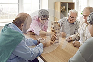Group of seniors playing together with wooden building blocks for dementia therapy in nursing home.