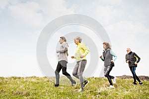 Group of seniors running outside on the green hills.