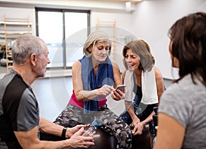 A group of seniors with smartphone in gym resting after doing exercise.